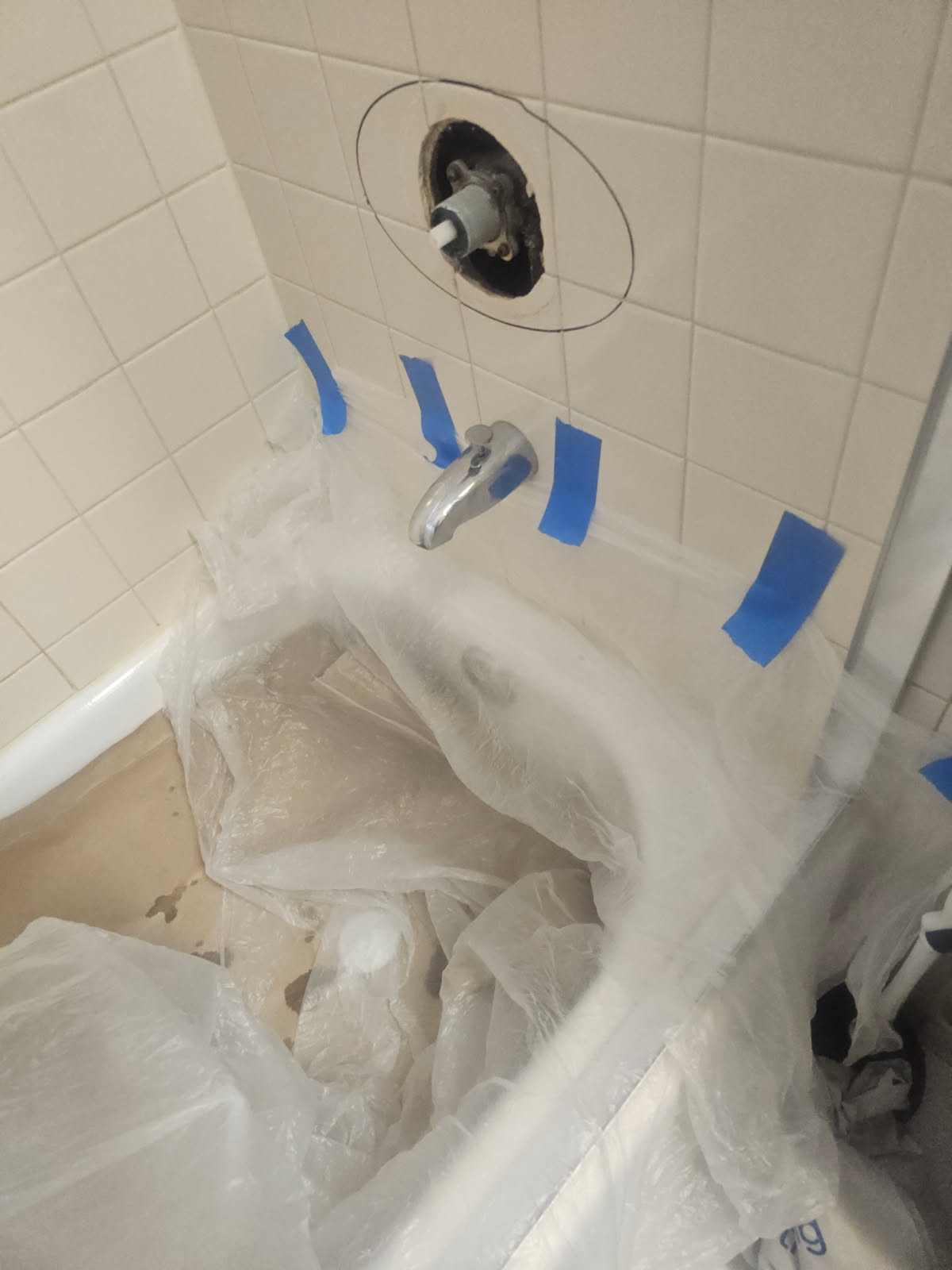 Tub area masked off with plastic and blue tape during a shower valve repair